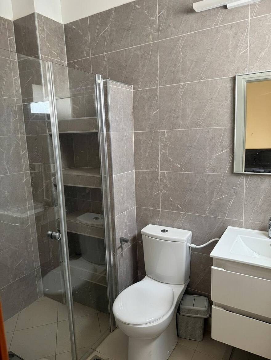 חדר רחצה עם מקלחון עם דלת זכוכית, מדפים בנישה, אסלה וארון כיור